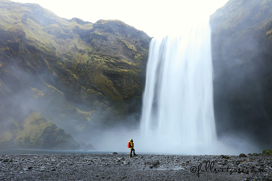 Hiker standing at a foot of a majestic Skogafoss Waterfall in Southern Iceland