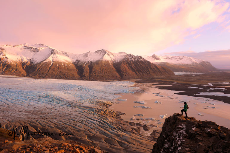 Hiker standing on a cliff at a glacier in Skaftafell National Park Iceland at sunset in winter