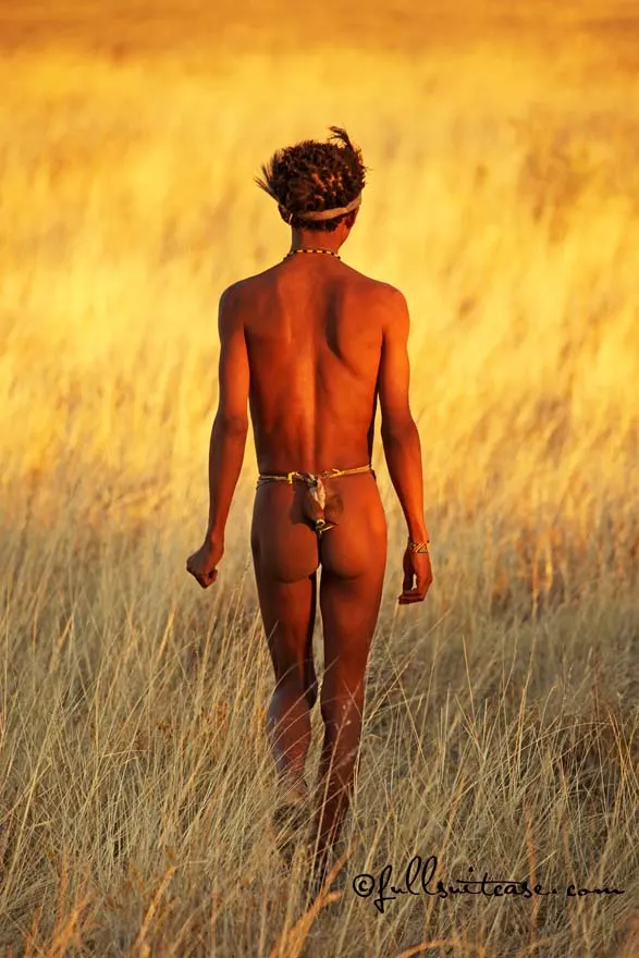 Male San hunter is walking in African savannah at sunset