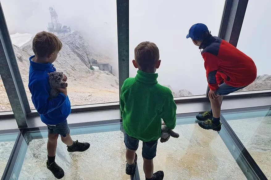 Kids standing on a glass floor overlooking the steep moutain at Zugspitze in Austrian Tirol