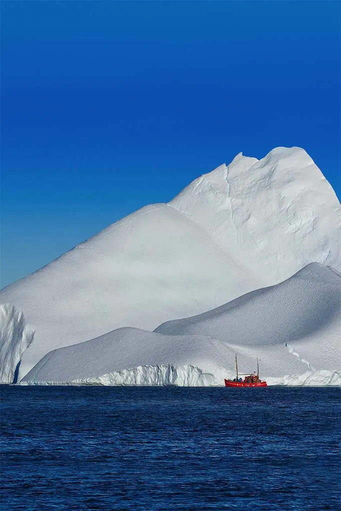 Small boat in front of a huge iceberg in Greenland