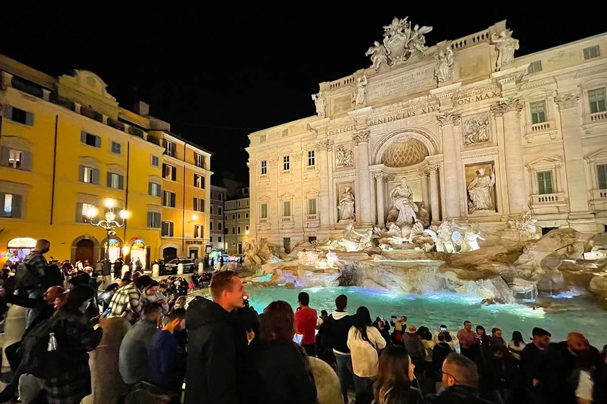 Fontana de Trevi por la noche con mucha gente a su alrededor.