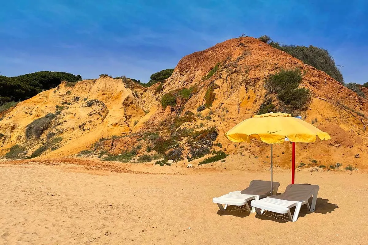 Beach chairs and yellow parasol with coastal cliffs background on Oura Beach in Albufeira