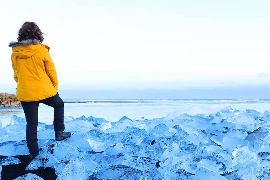 Woman wearing winter boots and warm yellow jacket on Diamond Beach in Iceland in winter