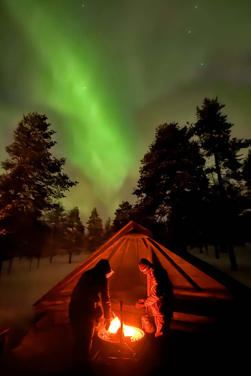 People warming by outdoor fire while watching the Northern Lights in Rovaniemi Finland