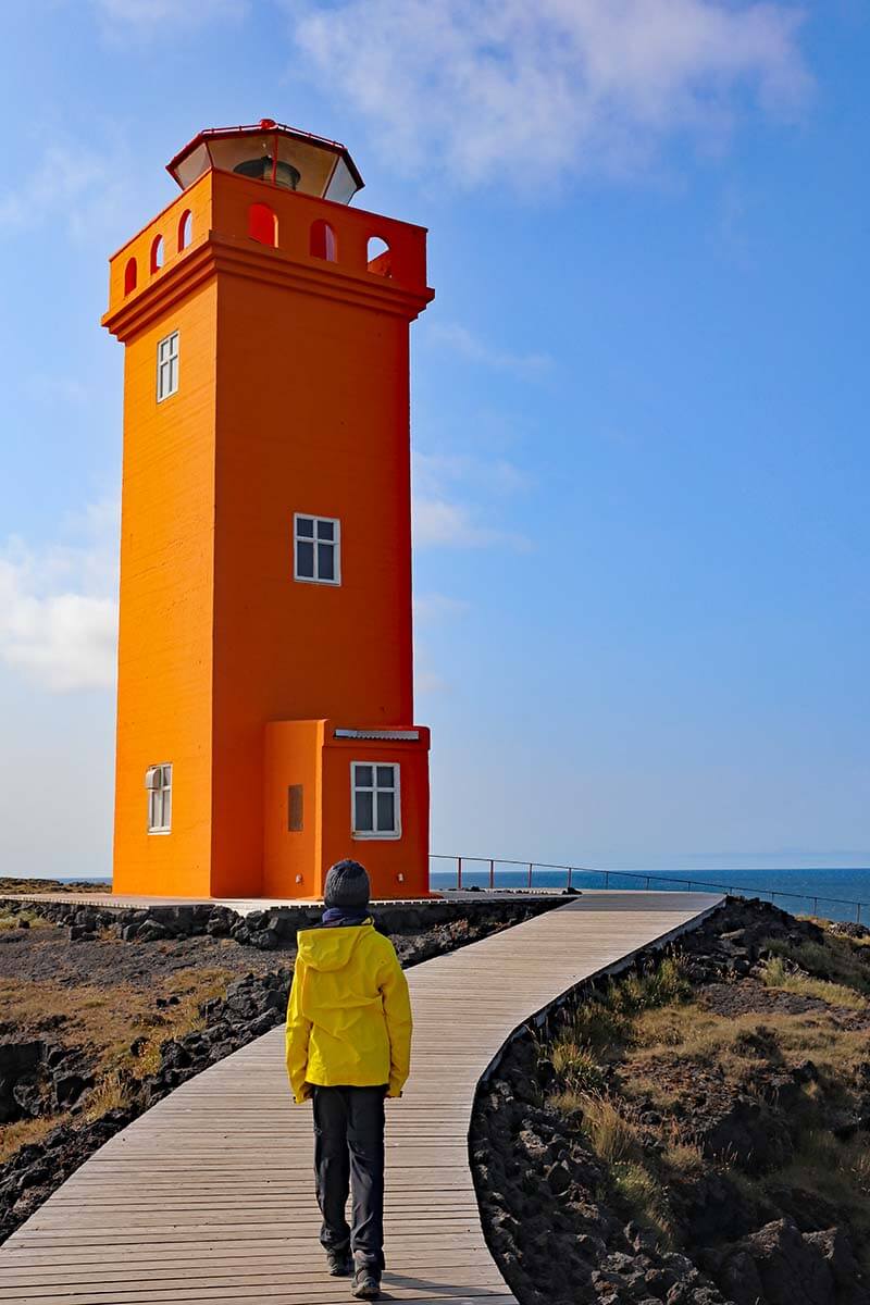 A teenager walking toward an orange lighthouse in Iceland