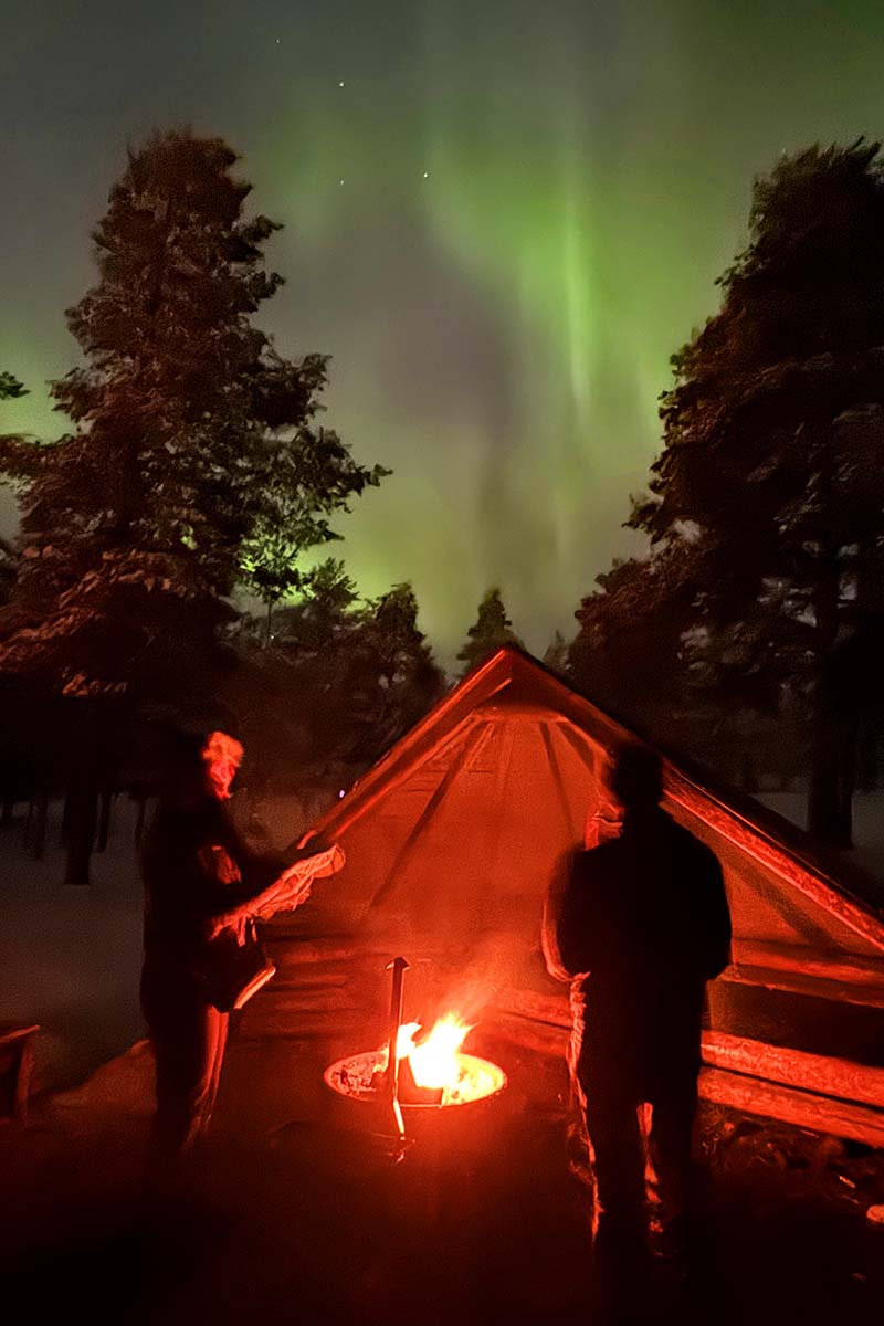 Teens by the outdoor fire watching the Northern Lights in Lapland Finland