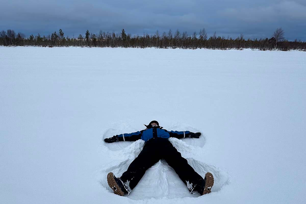 Teenager in a thermal overall making a snow angel on a frozen lake near Rovaniemi in Finland in winter