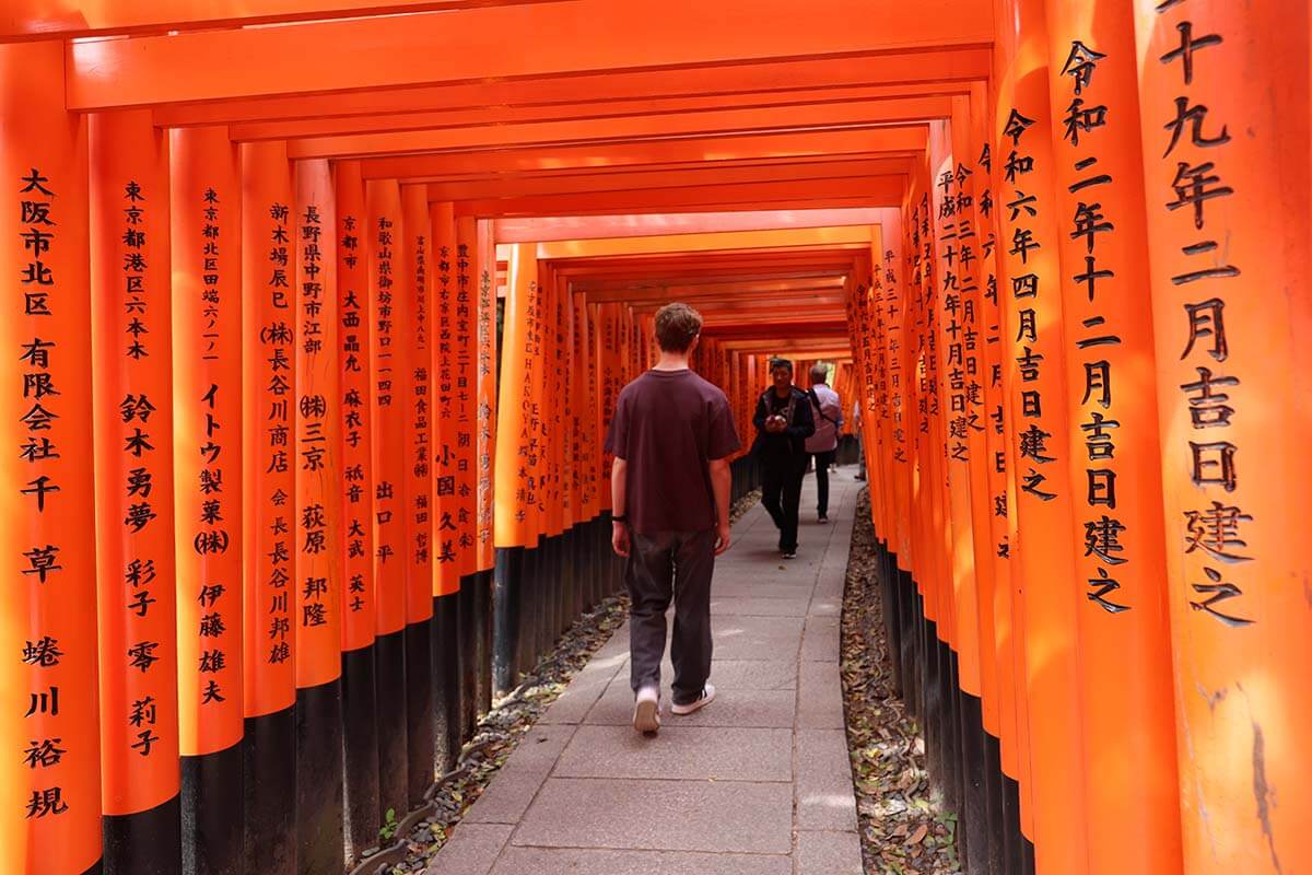 Teenager walking through orange Torii gates at Fushimi Inari Shrine in Kyoto Japan