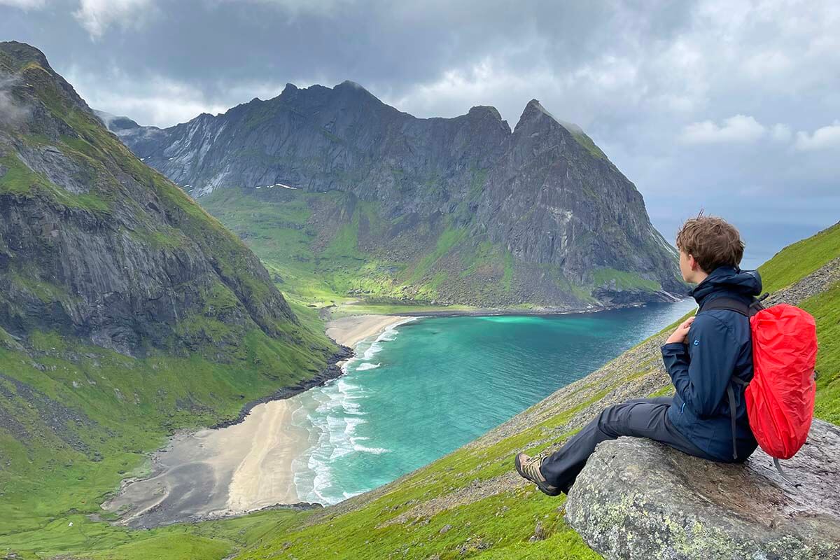 Boy hiking to Ryten in Lofoten with rain gear and a backpack protected by a rain cover