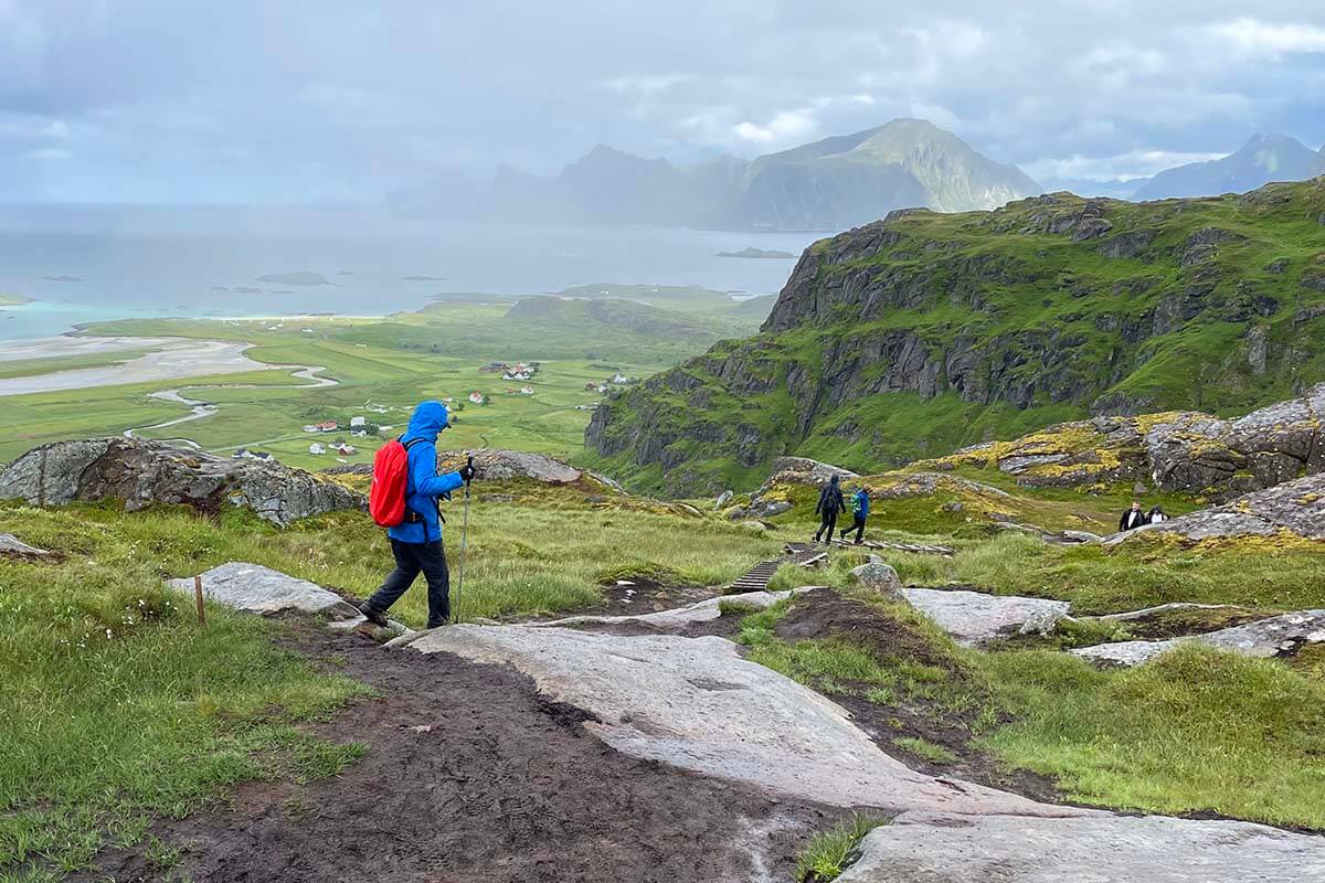 Hiker in rain gear and trekking poles walking on a muddy trail in Lofoten Islands in summer
