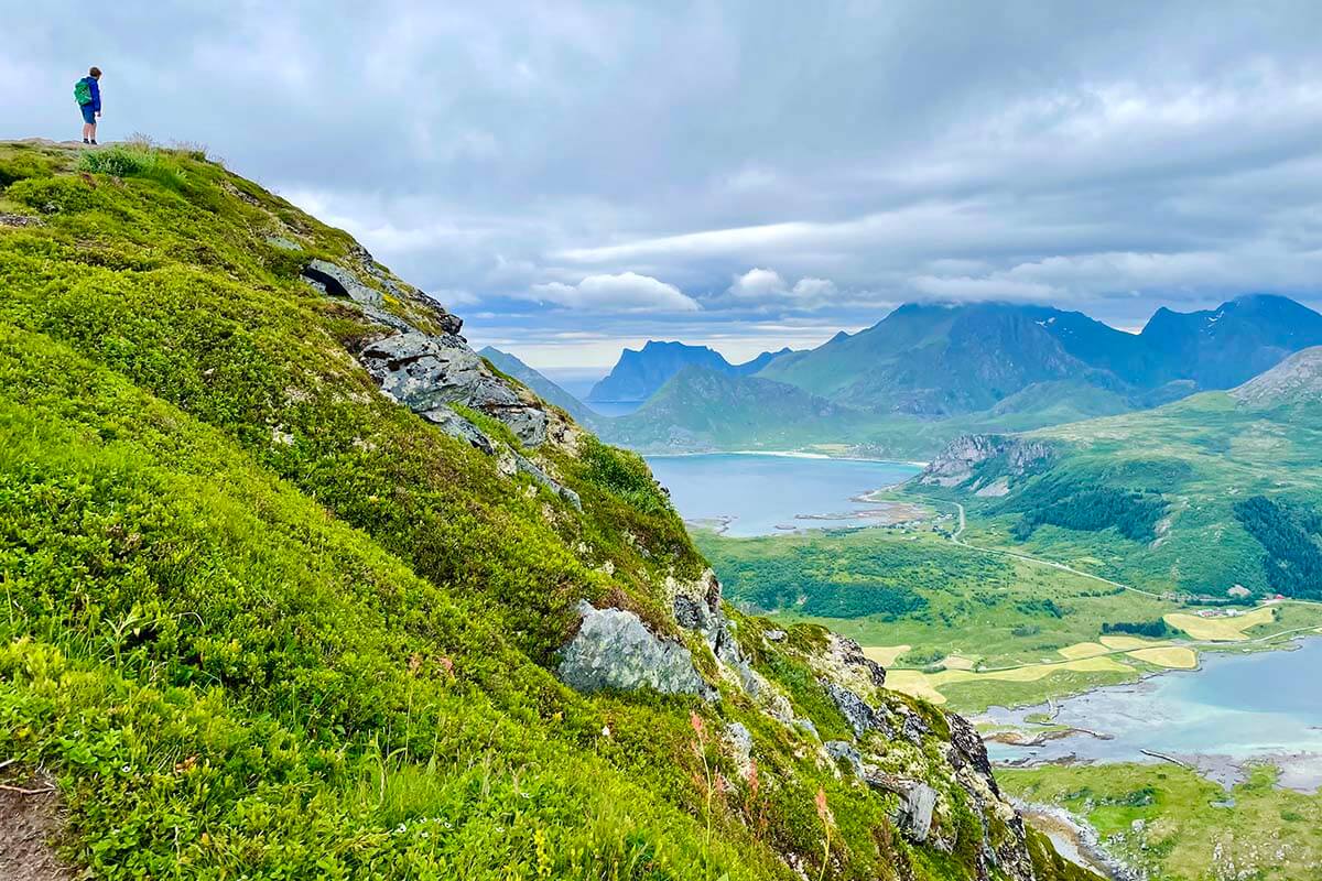 Hiker on the Offersøykammen trail overlooking mountains and coastline in the Lofoten Islands, Norway