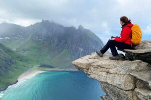 Hiker sitting on a rock above Kvalvika Beach on the Ryten hike in Lofoten, Norway