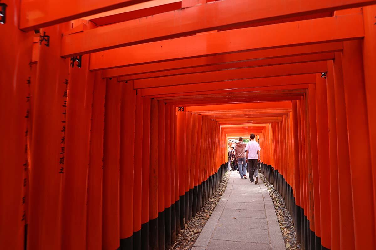 People walking under hundresd of orange torii gates at Fushimi Inari in Kyoto