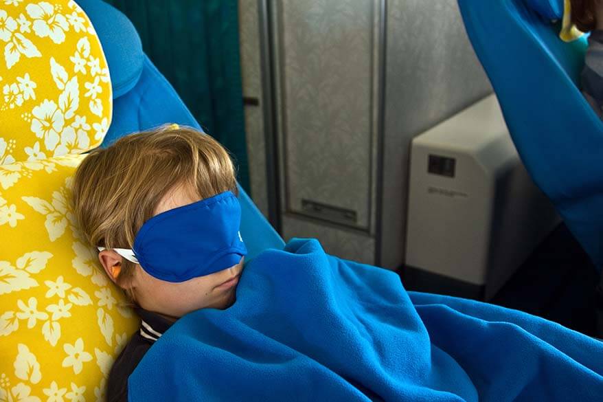 Child with a sleep mask and ear plugs sleeping on an airplane