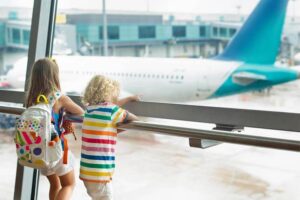 Flying with kids - children looking at the airplane through an airport window