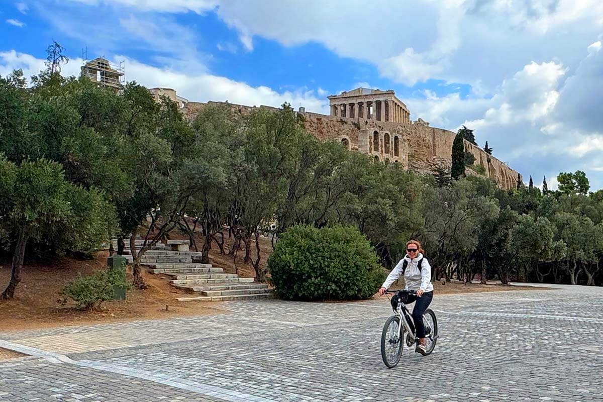 Tourist riding a bike in front of Acropolis on Athens bicycle tour