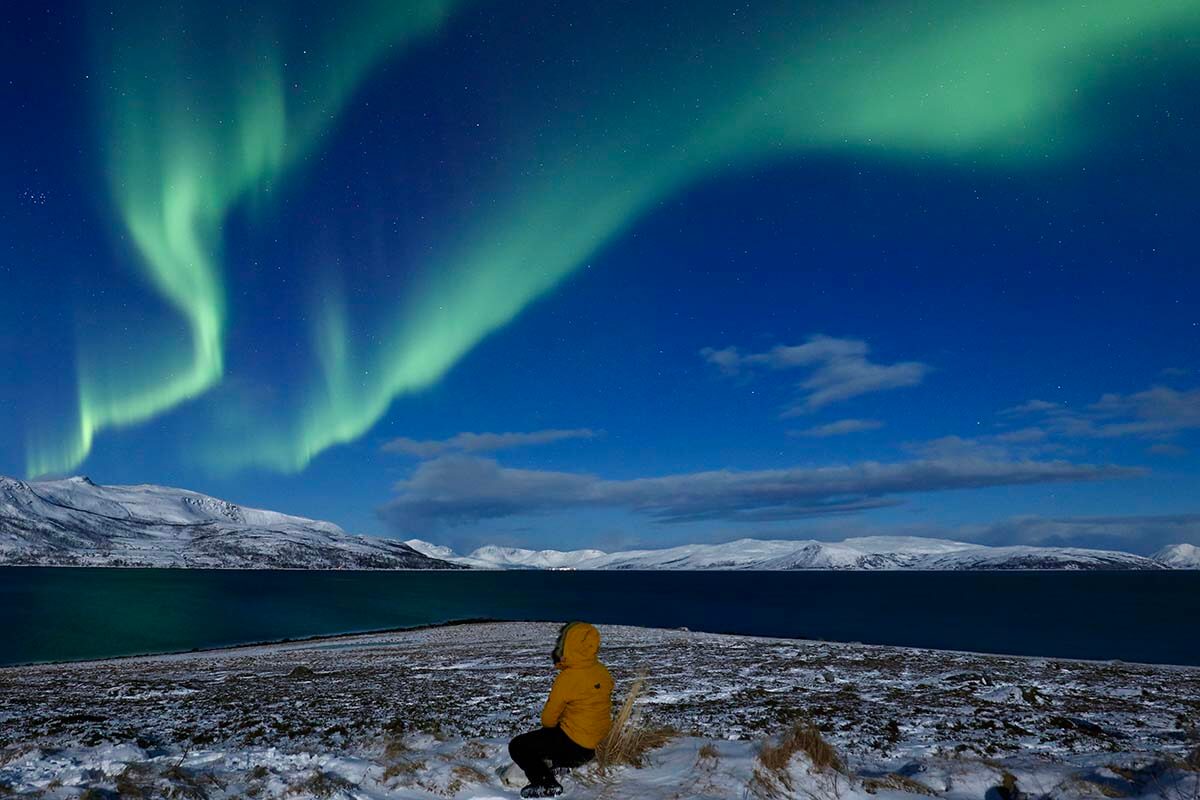 Woman looking at the Northern Lights surrounded by snowy fjords landscape in Tromso Norway